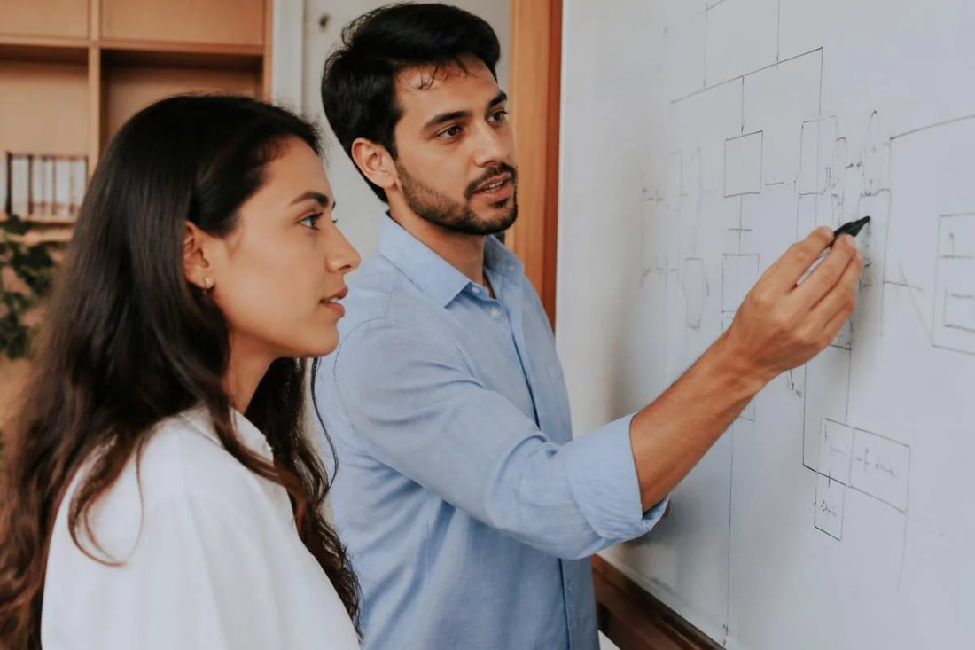 Facilitadora aponta para um mapa de argumento desenhado no quadro branco enquanto um participante acompanha